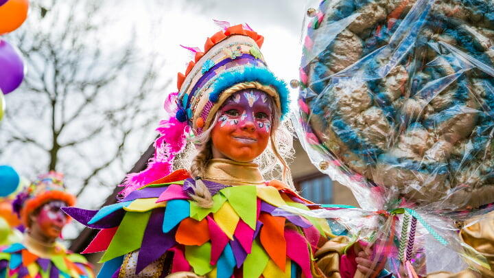Young child in fancy dress holding a gigantic lollipop at a Carnival celebration