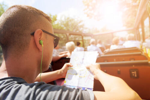 Man on an open top bus with headphones and a map