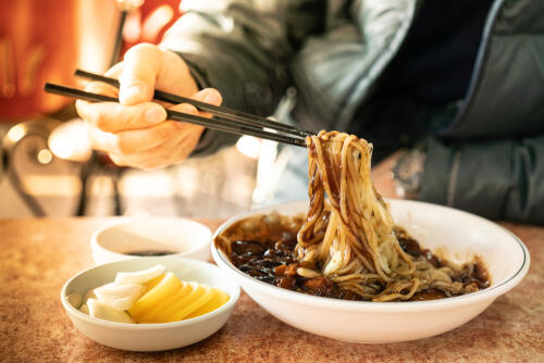 Bowl of black bean noodles being eaten with chopsticks