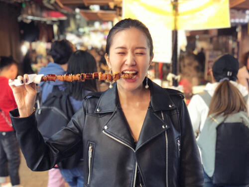 Woman eating meat on a stick at a night market in Seoul