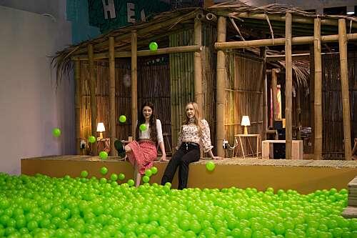 Two women sitting on the edge of a green ball pit