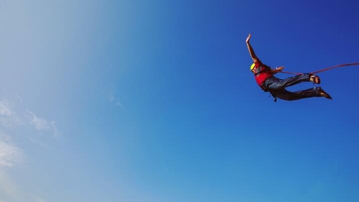 Bungee jumper free falling against a clear blue sky.