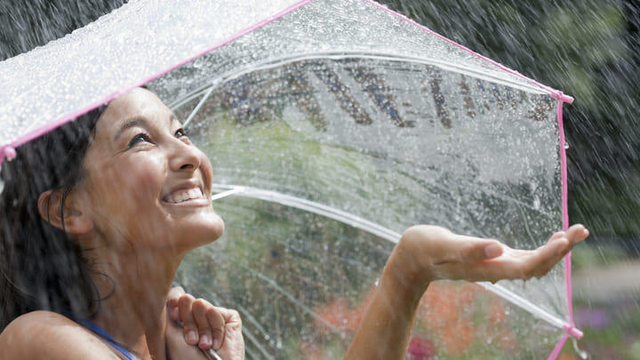 Woman laughing under an umbrella during a downpour.
