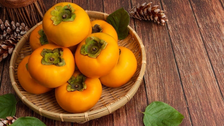 Ripe orange persimmons stacked in a bamboo bowl.