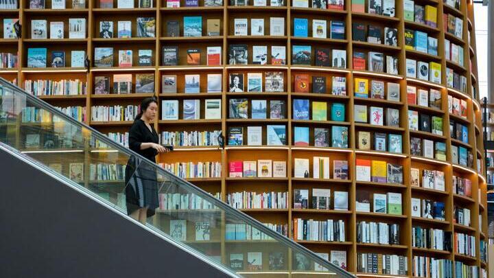 Woman on an escalator by a wall of books in the Starfield Library, Seoul.