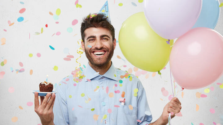Man celebrating his birthday with colorful balloons, confetti and a cupcake
