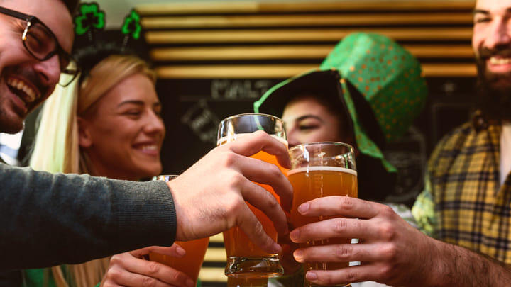 Drinkers in green headgear toast St Patrick's Day with pints in a bar