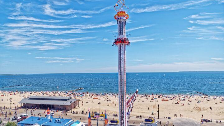 Astro Tower ride stands tall above the beach of Coney Island, against a blue sea and sky