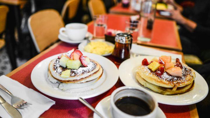 Table set with two plates of American pancakes, topped with fruit, plus maple syrup and coffee