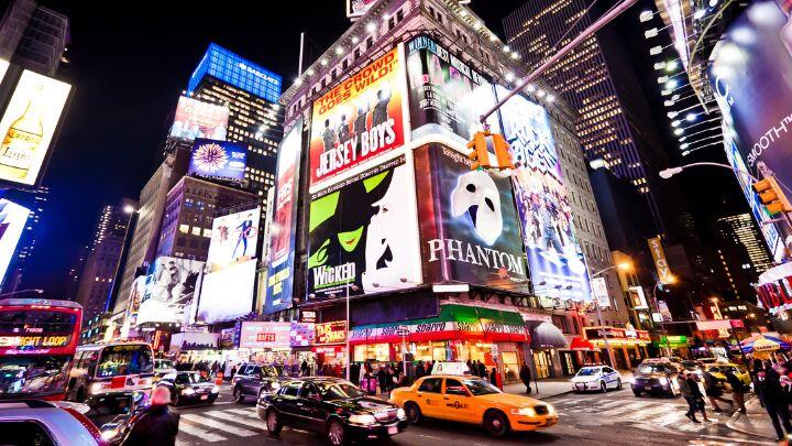 Times Square street corner featuring huge lit billboards for musicals including Wicked and Phantom