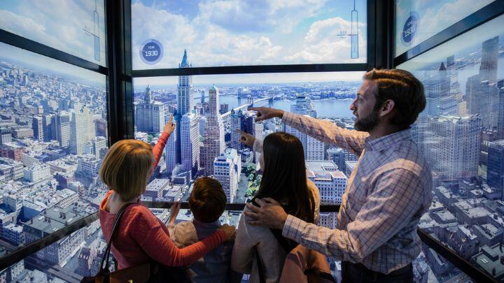 Family of four in glass elevator of One World Observatory pointing out New York landmarks