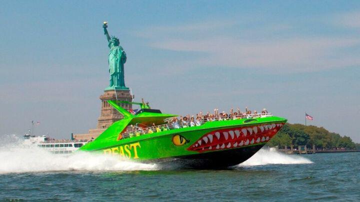Green speedboat painted to look like a monster throws up spray as it roars past the Statue of Liberty