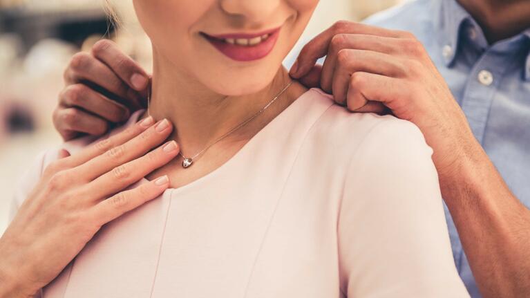 A man hangs a necklace around a woman's neck