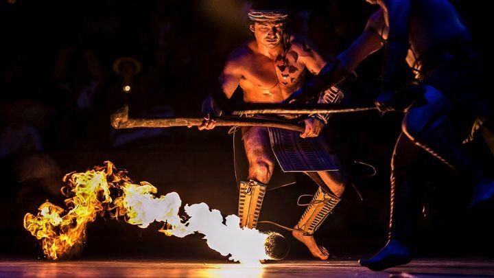 Mayan ball game player in traditional dress uses stick with flaming ball