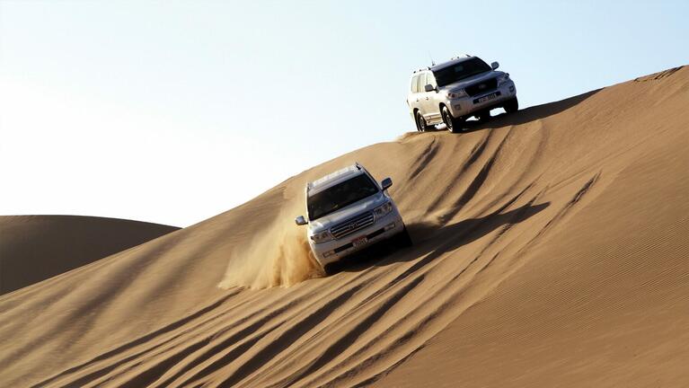 Two 4WDs driving over the top of a sand dune on a Dubai desert safari