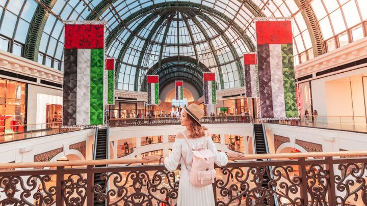 Woman looks out from balcony over Mall of the Emirates, with glass roof and hung with Emirates flags
