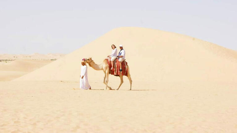 Visitors enjoying a camel ride beside the desert dunes of Dubai
