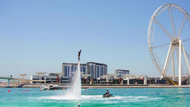 A flyboarder in the shallows in front of Ain Dubai observation wheel