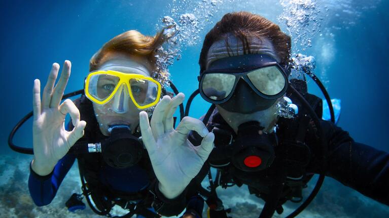 A pair of scuba divers making the okay sign underwater