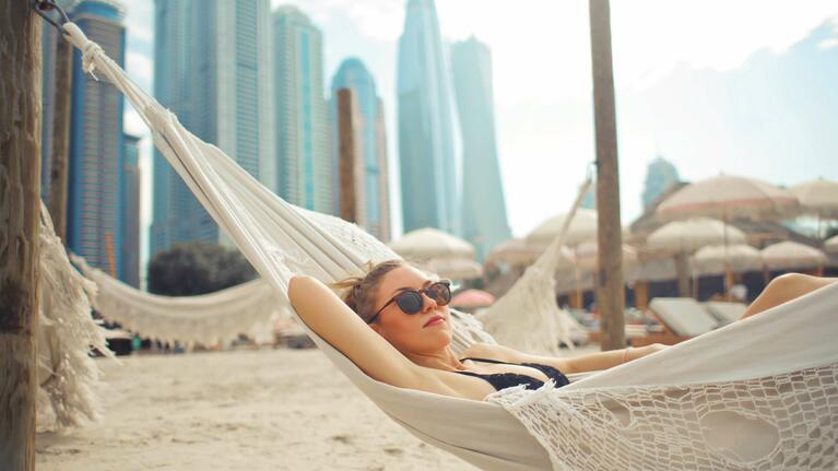 A young woman lies in a hammock with a backdrop of Dubai towers