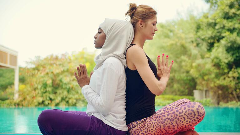 Two women back to back in yoga poses