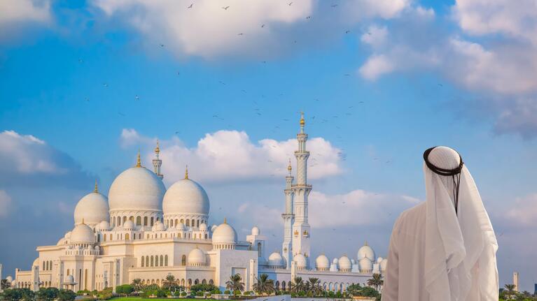 Blick auf eine Moschee in Dubai im Vordergrund ein Mann in traditioneller Bekleidung