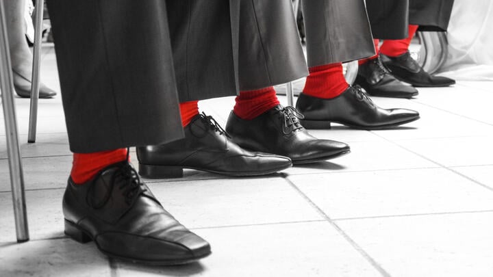 Three men wearing gray trousers, black shoes and bright red socks