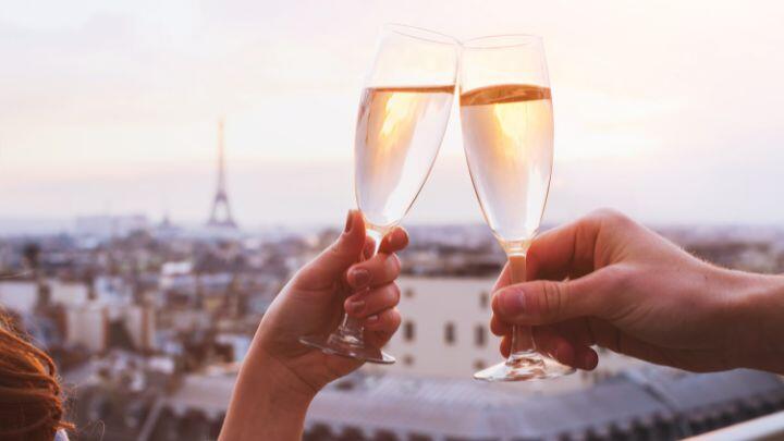 Hands holding champagne glasses raising a toast with background of Paris