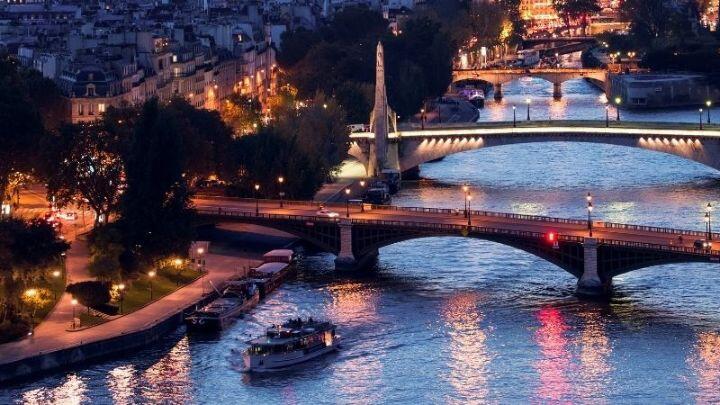Birds-eye view of River Seine showing cruise boat and bridges lit up in evening