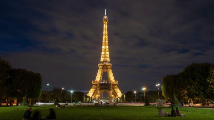 Illuminated Eiffel Tower, glowing against a night sky, with grass to front