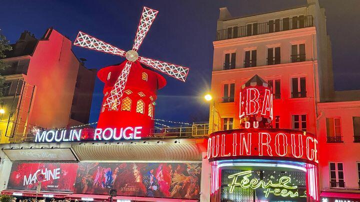 Exterior view of the windmill and frontage of Moulin Rouge, Paris, lit up red at night