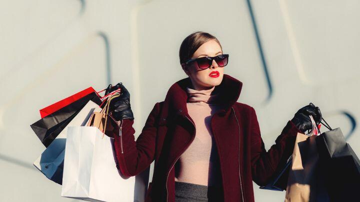 Stylish lady in sunglasses holding up both hands laden with high end shopping bags