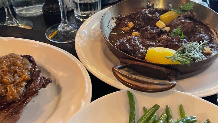 Plates and glasses on table, with boeuf bourgignon and partial view of steak and grean beans