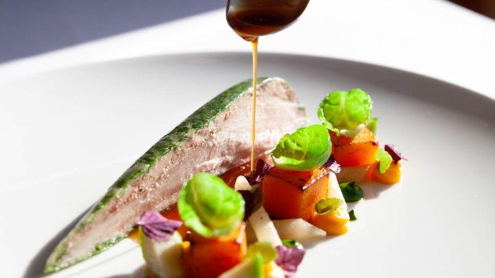 Jus is drizzled from a spoon over a minimal but brightly coloured and garnished plate of food