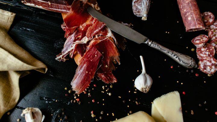 Overhead view of deli meat, sausage and cheese, with garlic and peppercorns on black surface