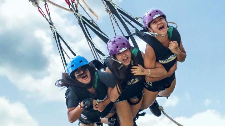 Three women in safety helmets swing towards the camera screaming and laughing