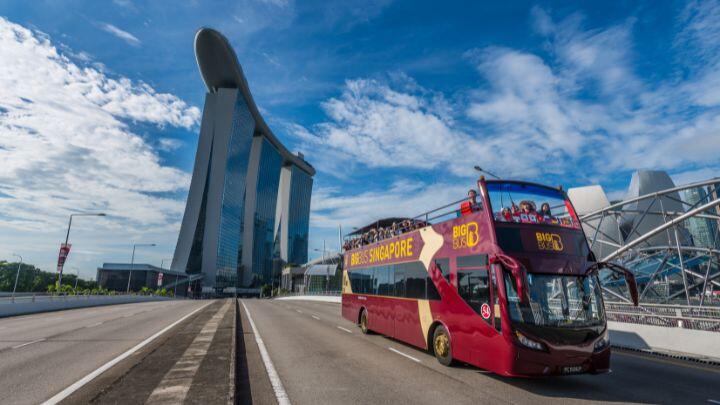 Dark red open top Big Bus on road with Marina Bay Sands hotel behind against blue sky