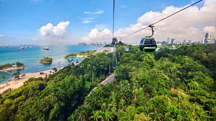 Singapore cable car suspended over lush vegetation with beach and blue sky behind