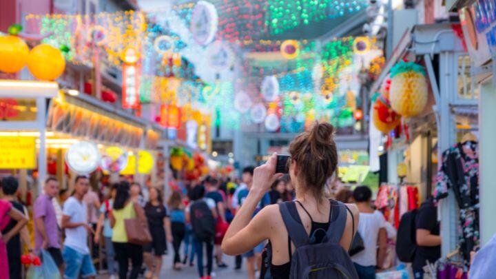 Female tourist with backpack takes a photo of the colourful lights and lanterns in narrow Singapore street