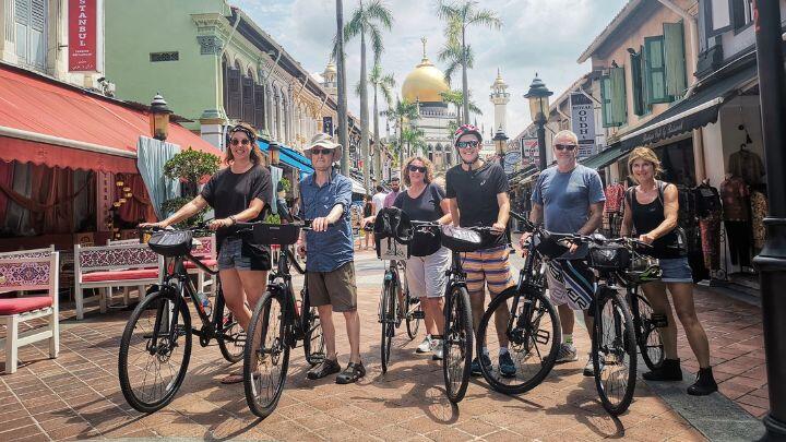 Group of people standing with bicycles in colourful Singapore street, with gold domed temple behind