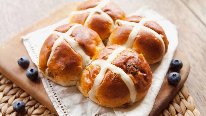 Four delicious looking hot cross buns on a napkin and board, garnished with blueberries