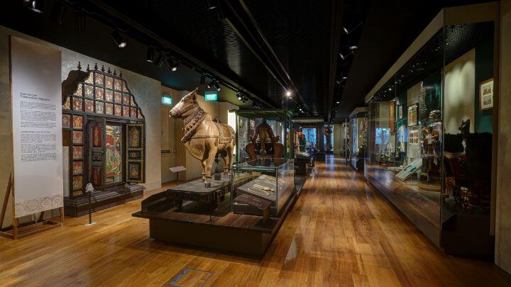 Glass cases and historic artefacts line a wood-floored room - Indian Heritage Centre Singapore
