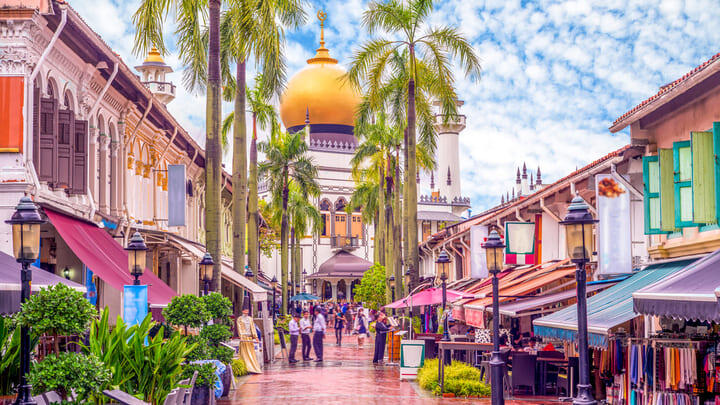 The colorful Kampong Glam district in Singapore, with the golden dome of the Sultan Mosque visible behind the palm trees.