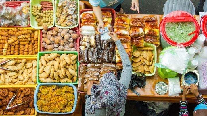 Overhead shot of colourful food products laid out on market stall, with trader serving a customer