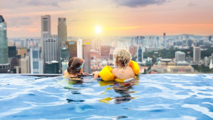 Back view of two children with swimming armbands at edge of infinity pool overlooking Singapore