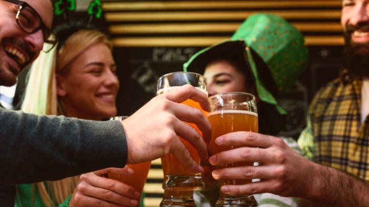 Close up of four people including woman with green leprechaun hat clinking pint glasses