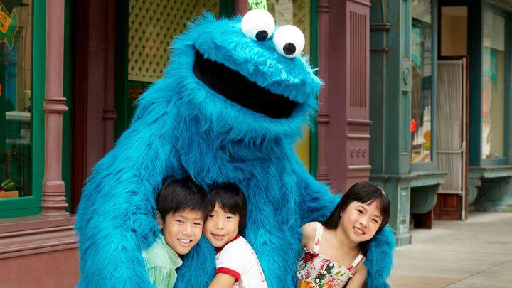 Sesame Streets blue hairy Cookie monster hugs three small children - Universal Singapore