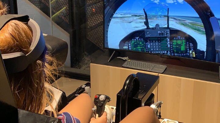 Over the shoulder view of woman in VR headset at the controls of a virtual jet fighter
