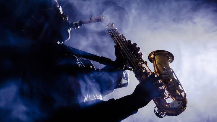 Person playing saxophone in a smoky jazz club.