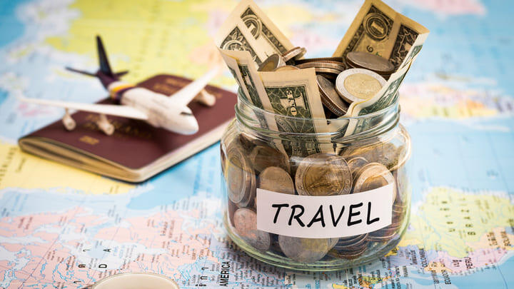 Jar of travel money sitting on a world map with a passport and model aeroplane.